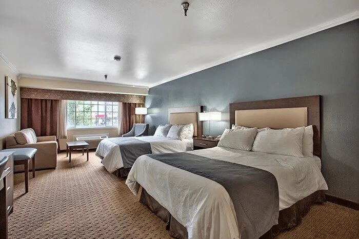 Hotel room interior featuring two queen beds, cozy seating area, and natural light from window, showcasing professional hotel portfolio by Listing Marketing Pros.