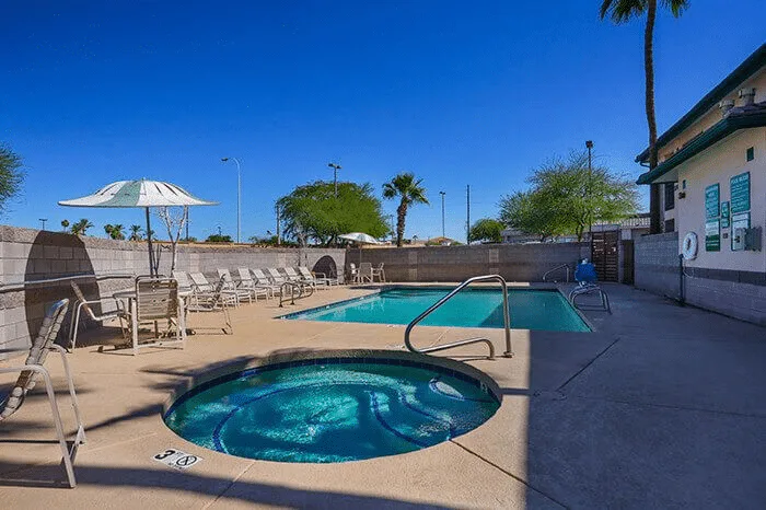 Hotel swimming pool area featuring a large pool and a hot tub, surrounded by lounge chairs and palm trees under a clear blue sky, showcasing the amenities of Listing Marketing Pros' hotel portfolio.